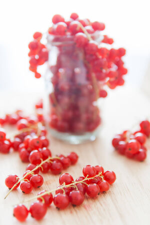 Redcurrant bunches in glass on light wood plate  Close-up photoの写真素材