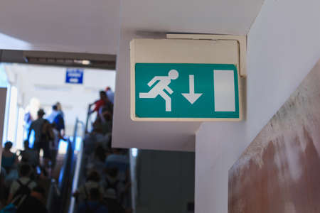 Emergency exit sign in corridor mounted on a wall. People walking in corridor backgroundの写真素材