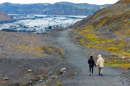 A couple holds hands and walks near the glacier tongue - Myrdalsjokull glacier.の写真素材