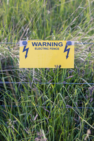 Warning - Electric fence guards a meadow and animals field. Summer season.の写真素材