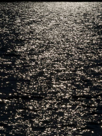Sunlight sparkles on the wavy sea at sunsetの写真素材
