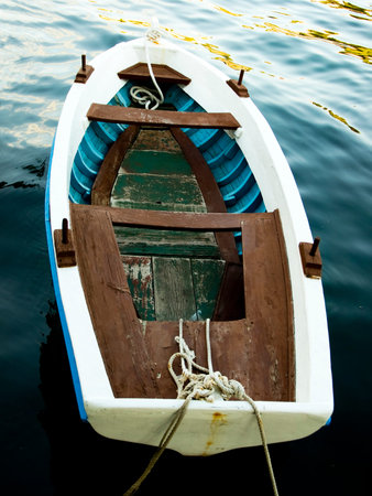 Small and old wooden boat alone on a clear blue sea.