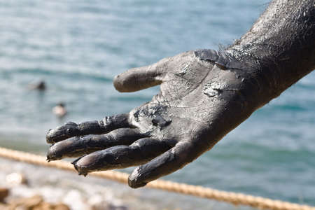 Hand covered with mud from Dead sea, Jordan. Skincare treatment. Use of high depth of field to blur the background.の写真素材