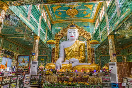 MANDALAY - FEBRUARY 26:  Golden sitting Buddha decorated with flowers in temple Sagaing Hill while the faithful pray on February 26, 2013 in Mandalay, Myanmar.のeditorial素材
