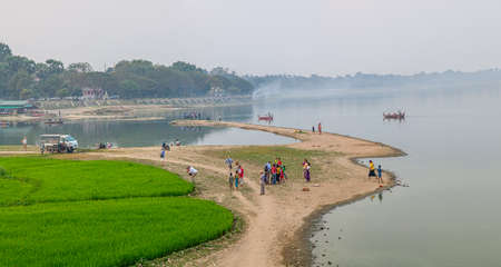 MANDALAY, MYANMAR - FEBRUARY 26, 2013: The view from the U-Bein bridge on the bank of the Irrawaddi river with people taking a leisurely stroll.のeditorial素材