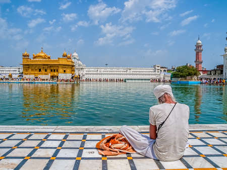 AMRITSAR, INDIA - MARCH 30, 2010: Sikh devotee sitting by the pool in front of the Golden Temple while Tourists and pilgrims entering  and walk towards The Harmandir Sahib Golden Temple, holiest shrine of the Sikh religion.のeditorial素材
