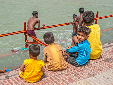 HARIDWAR, INDIA - APRIL 15, 2010: Children siting on the shore and watching the boys bathing by the holy river Ganga at the Kumbh Mela, a mass Hindu pilgrimage of faith.のeditorial素材