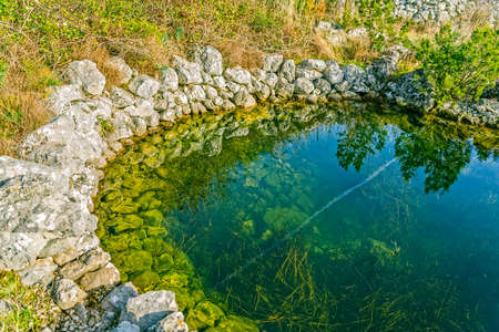 Ancient water trough with modern plane trail reflecting in the water at winter near village Oslje, Croatia.の写真素材