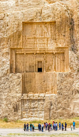 NAQSH-E RUSTAM, IRAN - MAY 3, 2015: The group of tourists with the tour guide in front of the historical monuments of ancient necropolis near ruins of old city Persepolis.のeditorial素材