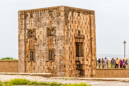 NAQSH-E RUSTAM, IRAN - MAY 3, 2015: The group of tourists with the tour guide checking out the Cube shaped construction Cube of Zoroaster, 5th century B.C.E. Achaemenid-era tower of ancient necropolis near ruins of old city Persepolis.のeditorial素材