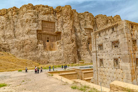 NAQSH-E RUSTAM, IRAN - MAY 3, 2015: The group of tourists with the tour guide checking out the Cube shaped construction Cube of Zoroaster, 5th century B.C.E. Achaemenid-era tower of ancient necropolis near ruins of old city Persepolis.のeditorial素材