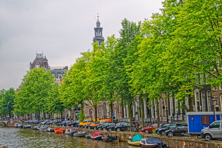 AMSTERDAM, NETHERLANDS - JUNE 11, 2016: Canal spring scene with green trees, boats and historic buildings.のeditorial素材