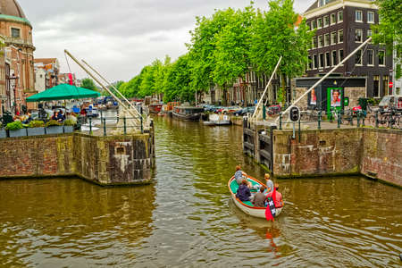 AMSTERDAM, NETHERLANDS - JUNE 11, 2016: Five young men sailing the Singel channel in a small boat by the Kopelkerk.のeditorial素材
