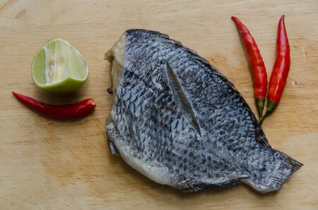 fresh fish with chillies and lemons on a wooden cutting boardの写真素材