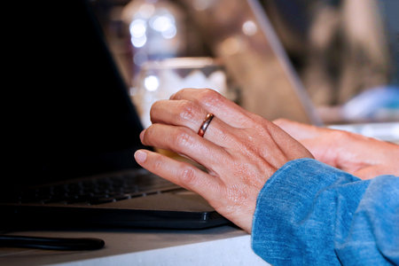 Close-up of woman's hands with wedding rings on laptop keyboardの写真素材