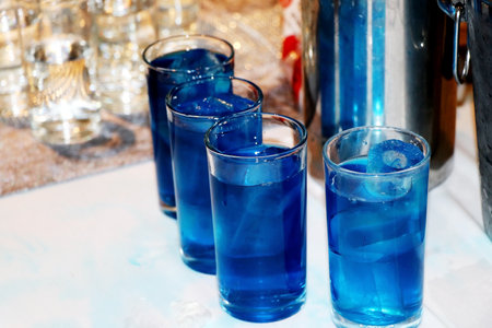 Blue drink in a glass with ice cubes on a blue background.の写真素材