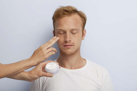 Portrait of young man being served with facial cosmetic treatment の写真素材