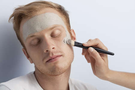 Portrait of young man being served with facial cosmetic treatment の写真素材