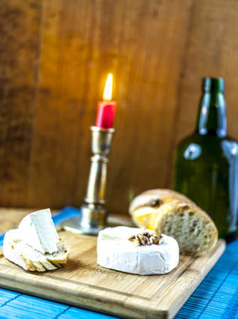 camembert and bread on wooden board with candle and bottle in the backgroundの写真素材