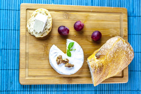 camembert, bread and dark grapes on wooden board from aboveの写真素材