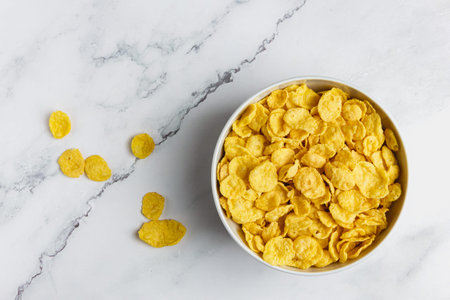 Corn flakes in white bowl on marble table. Top view of healthy breakfast.