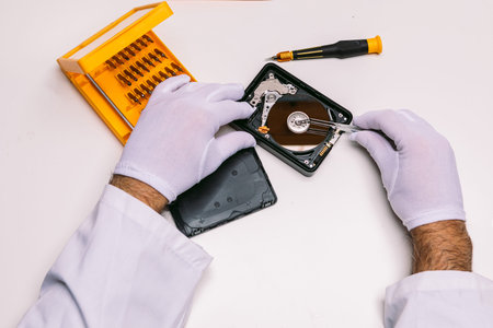 Hands of a technician with gloves repairing a hard drive. Technology maintenance concept