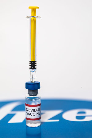 MADRID, SPAIN - JAN, 25, 2021: Vial filled with Covid-19 vaccine and syringe over the Pfizer logoのeditorial素材