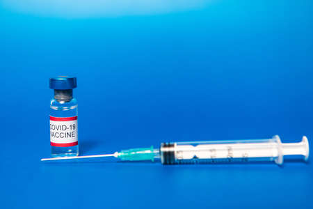 Vial with filled with Covid-19 vaccine and syringe on blue backgroundの写真素材