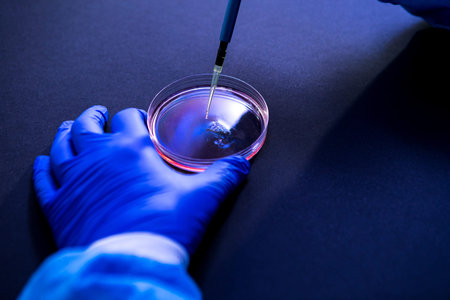Scientist pipetting a drop of fluid into a petri dish in a laboratory