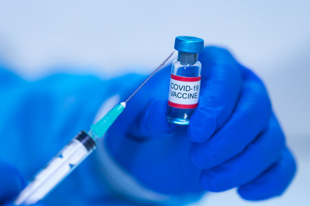Vial with the vaccine for COVID-19 held by the hand of a doctor and in the other hand a syringe. Coronavirus vaccination conceptの写真素材