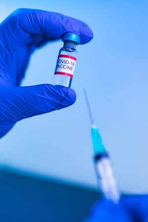 Vial with the vaccine for COVID-19 held by the hand of a doctor and in the other hand a syringe....