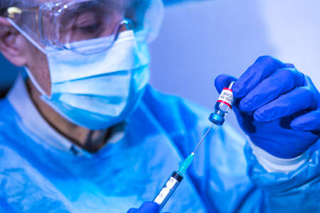 Doctor inserts the needle of a syringe into the vial with the COVID-19 vaccine to extract the liquid to vaccinate. Coronavirus vaccination conceptの写真素材
