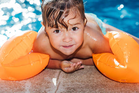Little blond-haired girl in the pool wearing sleeves, smiling and looking at cameraの写真素材