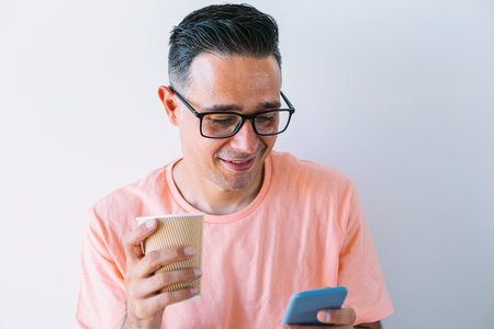 Man teleworking from home, looking at the mobile while having a coffee breakfast