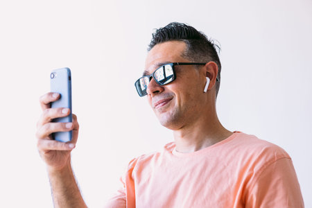 Man teleworking from home, wearing headphones and sunglasses, looking at mobile phone