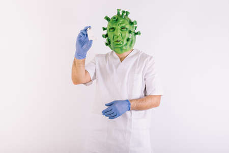 Person disguised as  virus with latex mask -   virus, wearing doctor's suit, holding large syringe, on white background.の写真素材