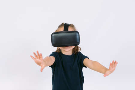 Little girl wearing virtual reality glasses with hands trying to touch something virtually, on white backgroundの写真素材