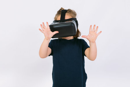 Little girl wearing virtual reality glasses with hands trying to touch something virtually, on white backgroundの写真素材