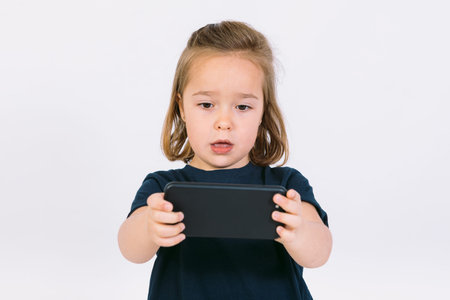 Little blonde girl with mobile phone in her hands, playing a gameの写真素材