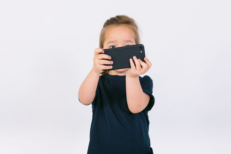 Little blonde girl with mobile phone in her hands, playing a gameの写真素材