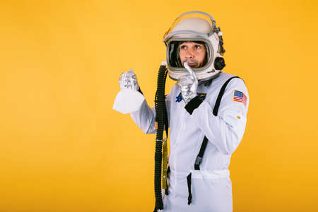 Male cosmonaut in spacesuit and helmet, holding a FPP2 mask, on yellow background.  virus conceptの写真素材