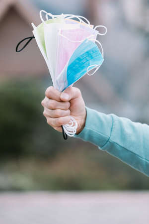 Detail of an arm holding a handful of colored surgical masks. Covid-19 conceptの写真素材