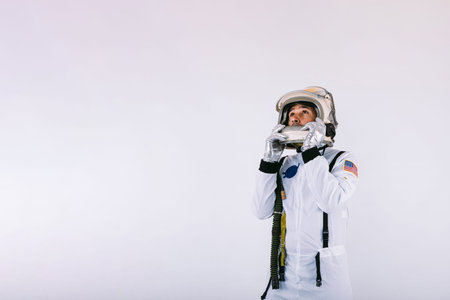 Male cosmonaut in space suit and helmet, holding helmet with hands, on white background.の写真素材