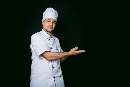 Chef cook wearing jacket and kitchen hat pointing right on black backgroundの写真素材