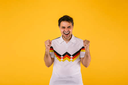 Soccer fan wearing a white t-shirt with black, red and yellow stripes, poses with crossed armsの写真素材