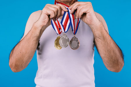 Elderly athlete with sun marks on his arms, with three medals on his neck, teaching them, on blue...