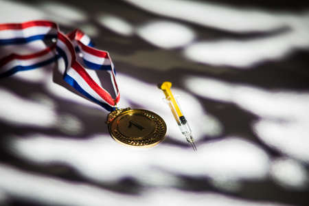 Gold medal and champion's cup, syringe with doping substance, pill tablet and vial with prohibited substance with lights and shadows of a curtain entering through the window. Sport and doping conceptの写真素材