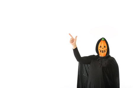 Person dressed in pumpkin Jack-o.-lantern mask and hooded velvet cape, pointing fingers up with copy space, on white background. Carnival, Halloween and Day of the Dead concept.の写真素材