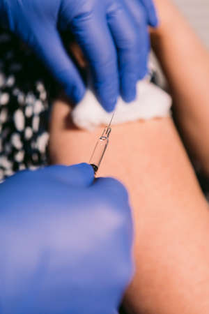 Nurse disinfects an older woman's arm with cotton to inject a vaccineの写真素材