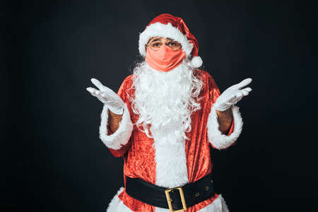 Man dressed as Santa Claus wearing a red mask and disgruntled gesture, on black background. Christmas concept, Santa Claus, gifts, celebration.の写真素材